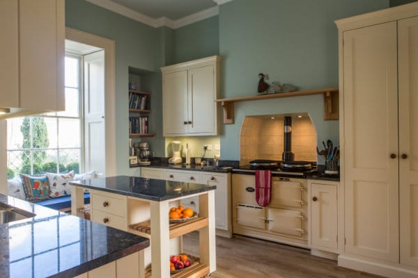 Wide view of a kitchen showing Aga range cooker, window seat and mobile kitchen island with granite worktop